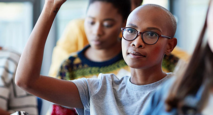 black woman with short hair and glasses raising her hand in a health education class
